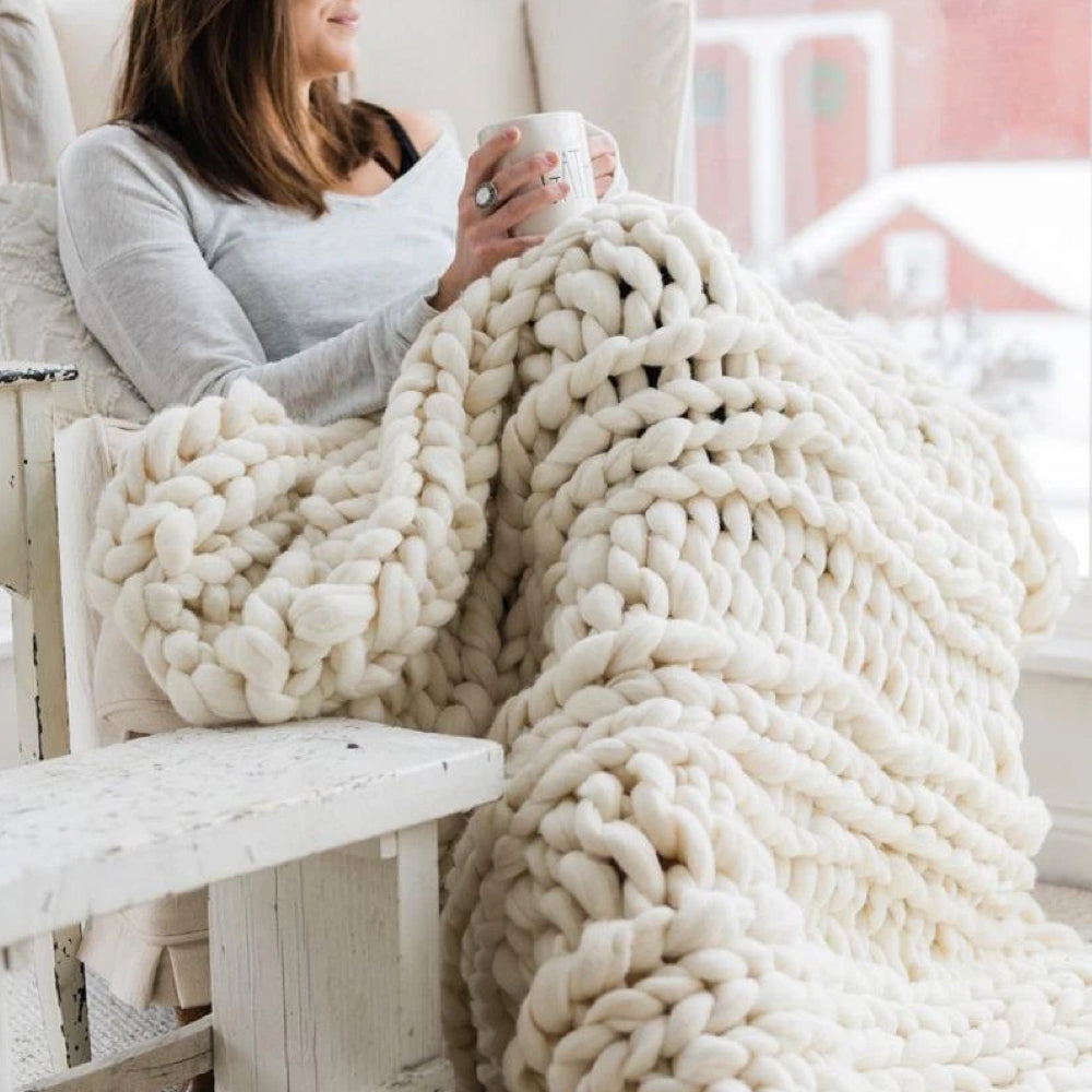 Frau mit weißer, grob gestrickter Decke aus Wolle, gemütlich auf Sofa, Winter, Innenraum.