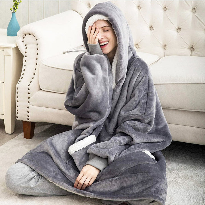 Frau in grauem, flauschigem Hoodie-Decke auf Sofa, gemütlich, warm, Winterkleidung.