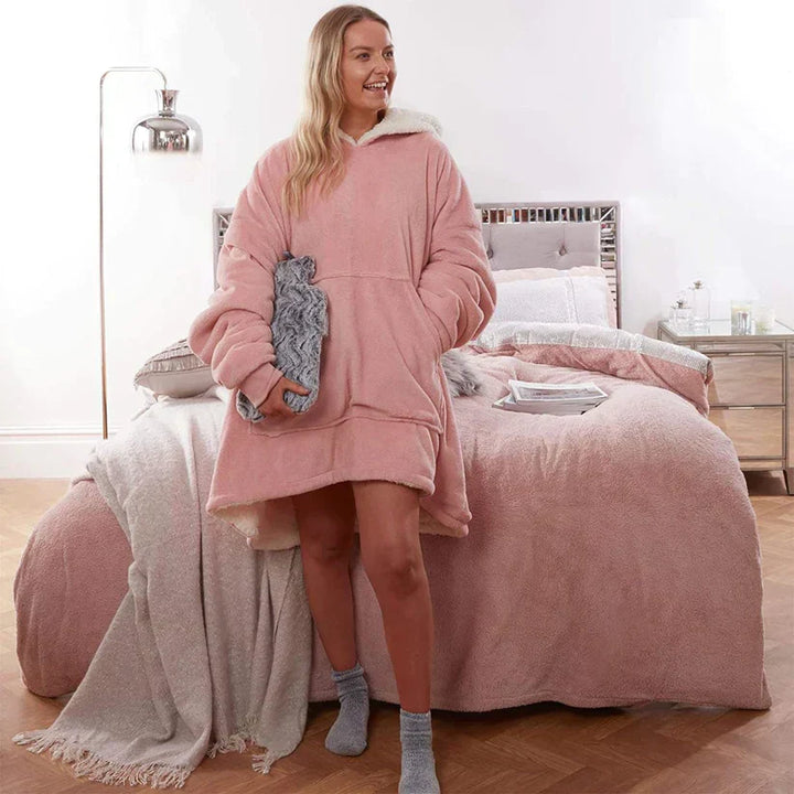 Frau in rosa Oversize-Kapuzendecke im Schlafzimmer, gemütliche Winterkleidung, weiches Fleece.