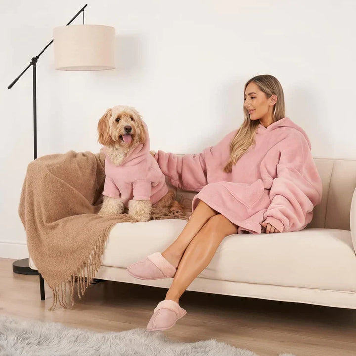 Frau und Hund in rosa Kuscheldecken auf Sofa, gemütliches Wohnzimmer, moderne Einrichtung.