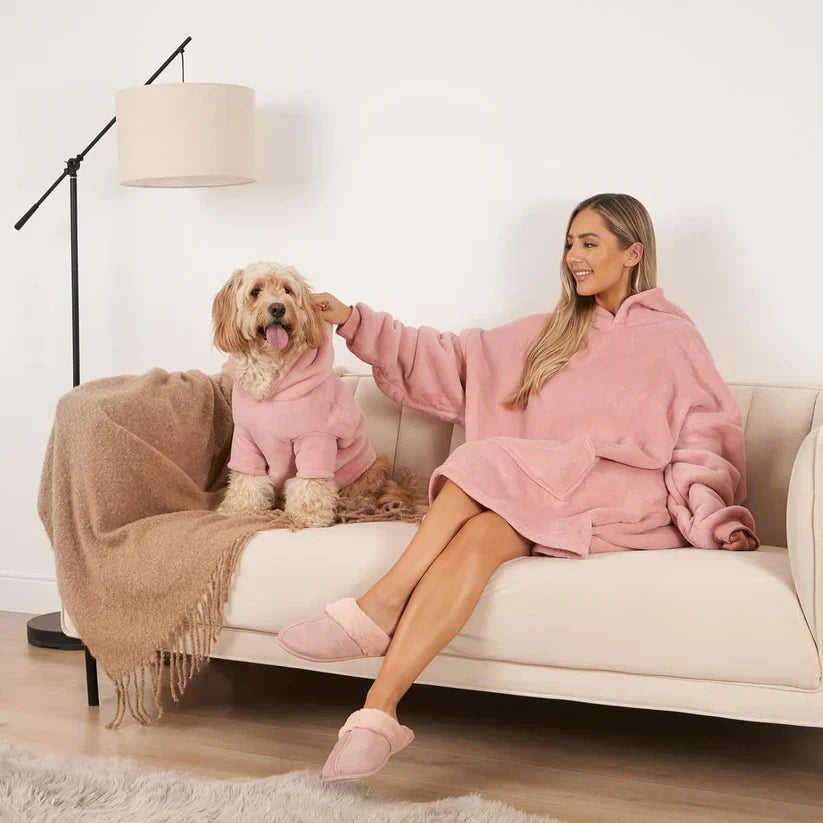 Frau und Hund in rosa Kuscheldecken auf Sofa, gemütliches Wohnzimmer, moderne Stehlampe.