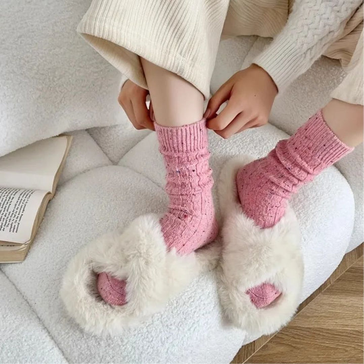 Frau mit rosa Socken und weißen Plüschpantoffeln auf einem weißen Sofa, gemütliche Wintermode.