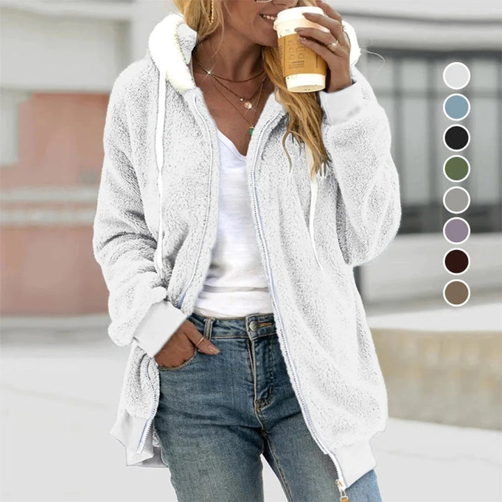 Frau in weißer Fleecejacke mit Kapuze, hält Kaffeebecher, lässige Mode, Herbstbekleidung.