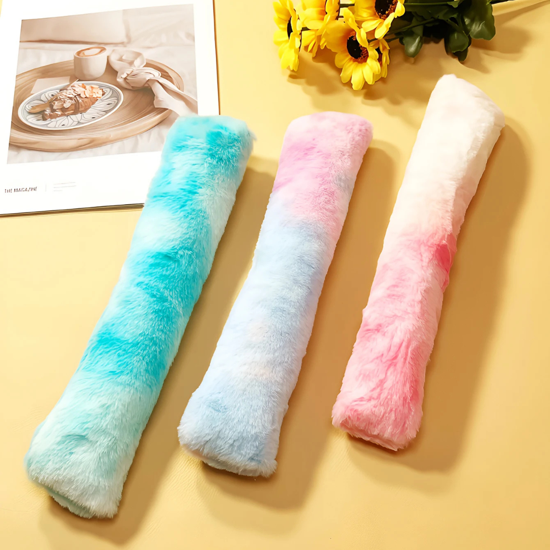 Drei flauschige, bunte Plüschkissen in Blau, Rosa und Weiß auf gelbem Hintergrund.