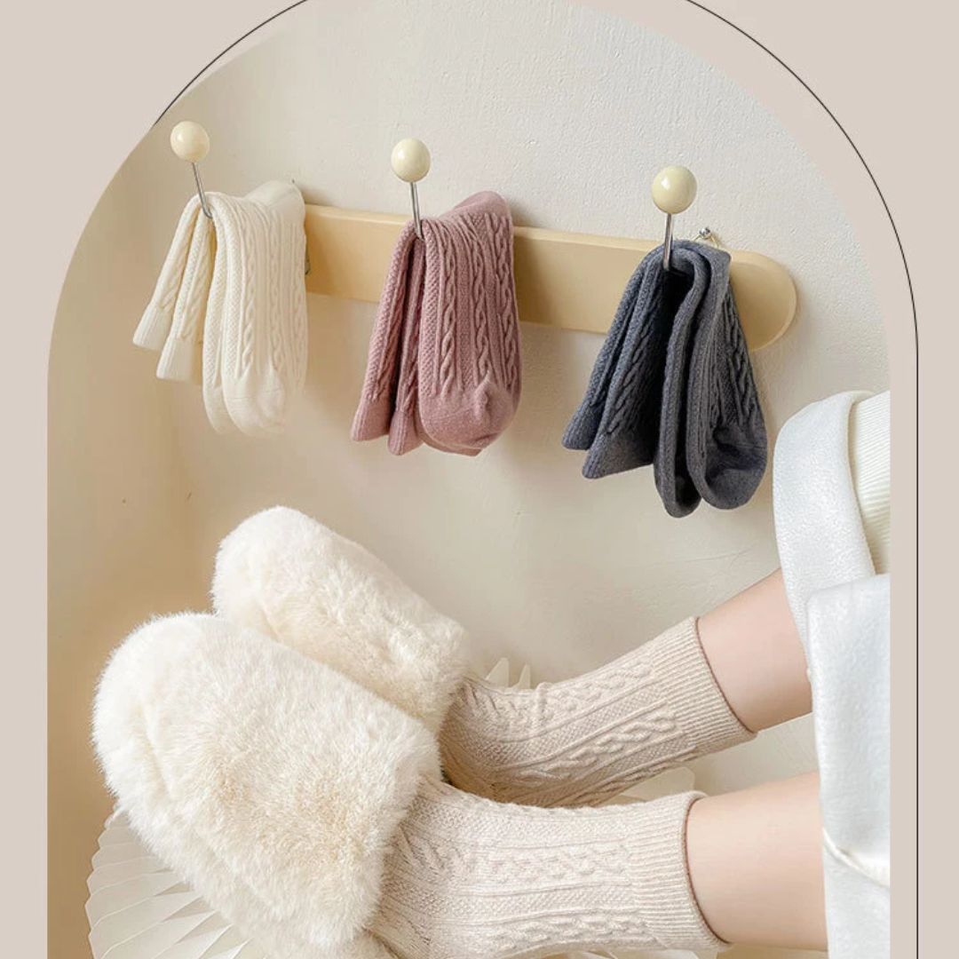 Warme Stricksocken und flauschige Hausschuhe in Creme, Rosa und Grau auf Haken.