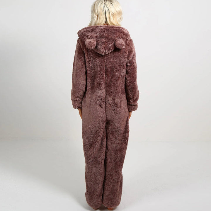 Frau in braunem Plüsch-Onesie mit Kapuze und Bommeln, gemütliche Nachtwäsche.