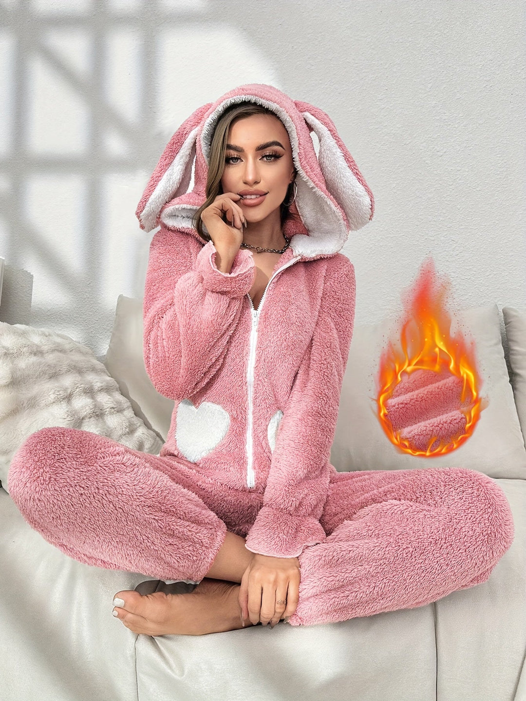 Frau in rosa Plüsch-Hasen-Einteiler mit Kapuze, Herzmuster, gemütlich, auf Sofa sitzend.