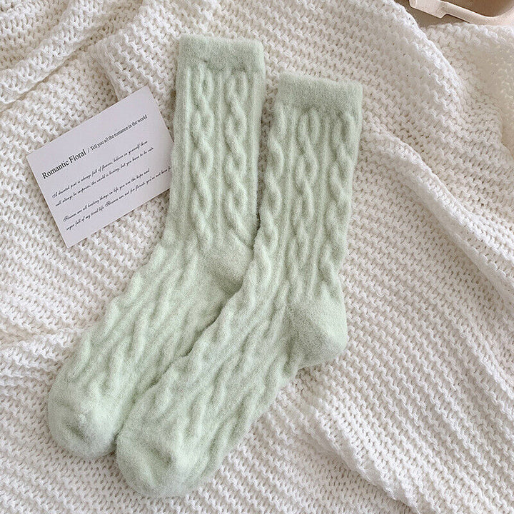Weiche, grüne Stricksocken auf weißem Strickhintergrund, gemütliche Wintermode.