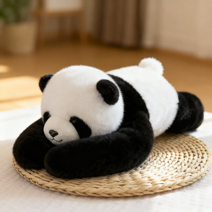 Černobílá plyšová panda s dlouhýma pažema leží natažená na slaměné podložce v útulném interiéru. 1