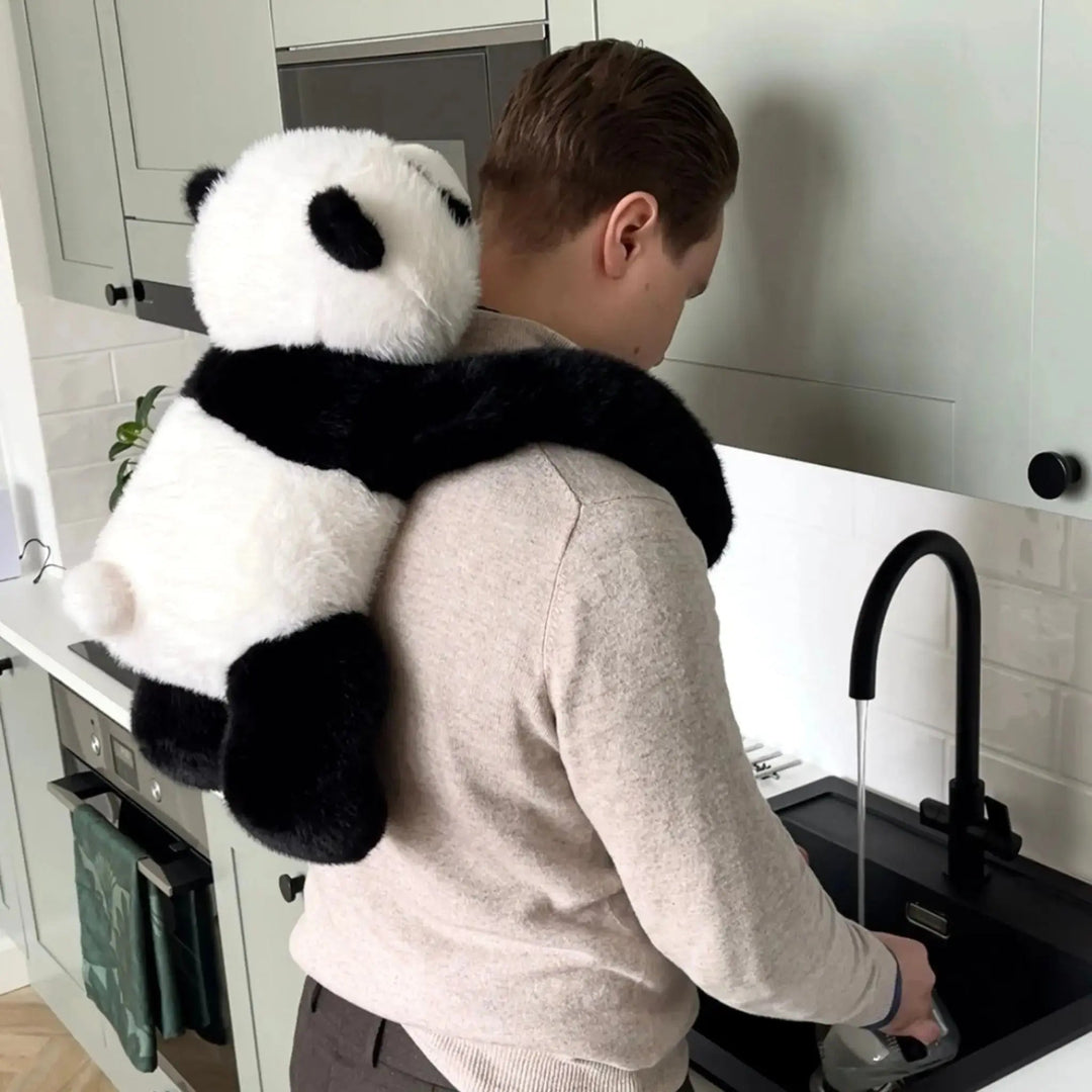 Muž u kuchyňského dřezu nosí pandu na zádech, její dlouhé paže mu obepínají ramena, zatímco myje nádobí. 10