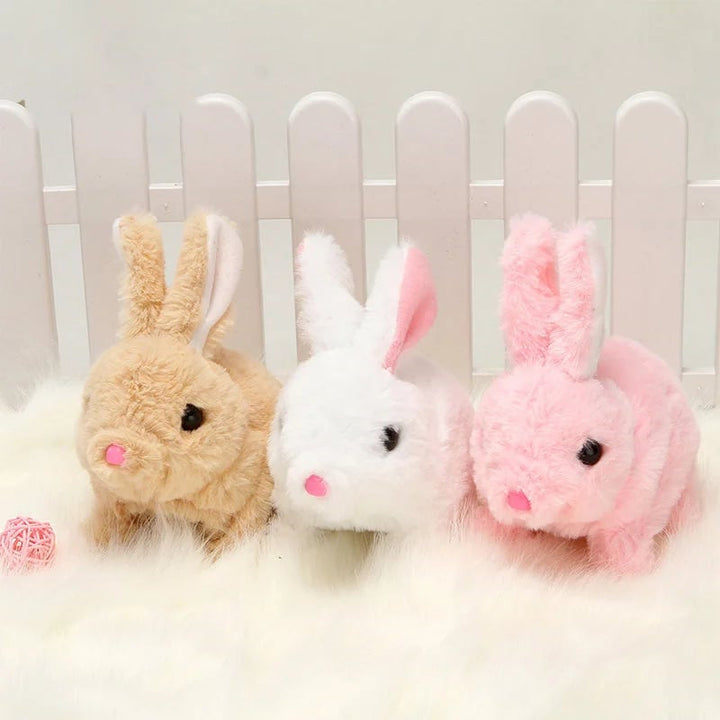 Drei Plüschhasen in Beige, Weiß und Rosa vor weißem Zaun auf flauschigem Teppich.