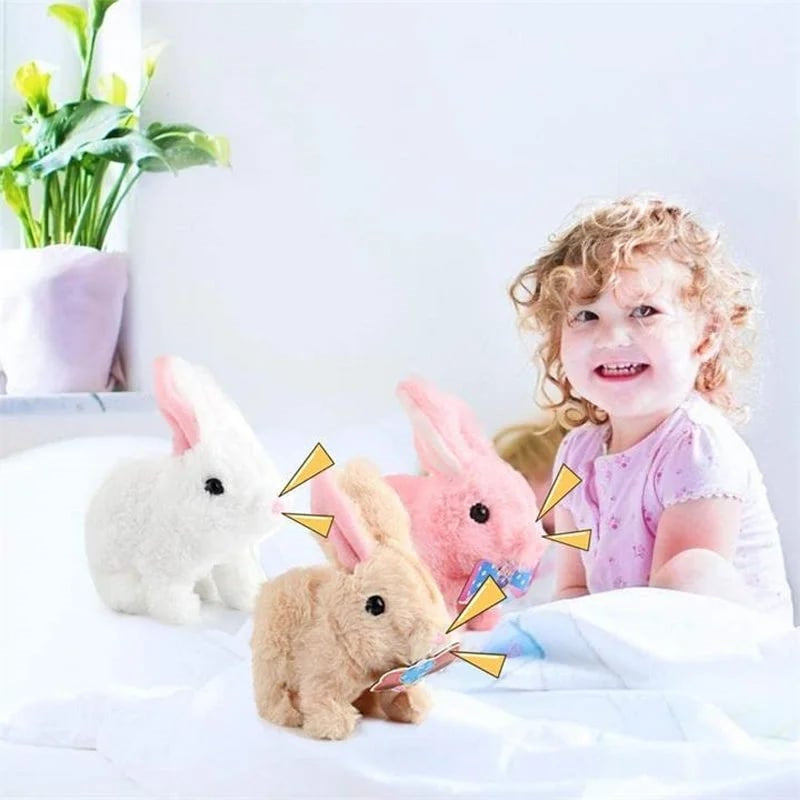Kleinkind mit drei Plüschhasen in Weiß, Rosa und Beige auf weißem Bett, lächelnd.