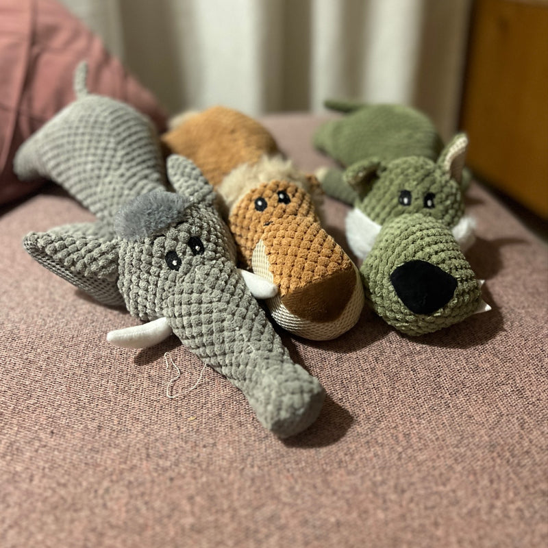 Drei gestrickte Hundespielzeuge in Elefanten-, Fuchs- und Hundedesign auf rosa Sofa.