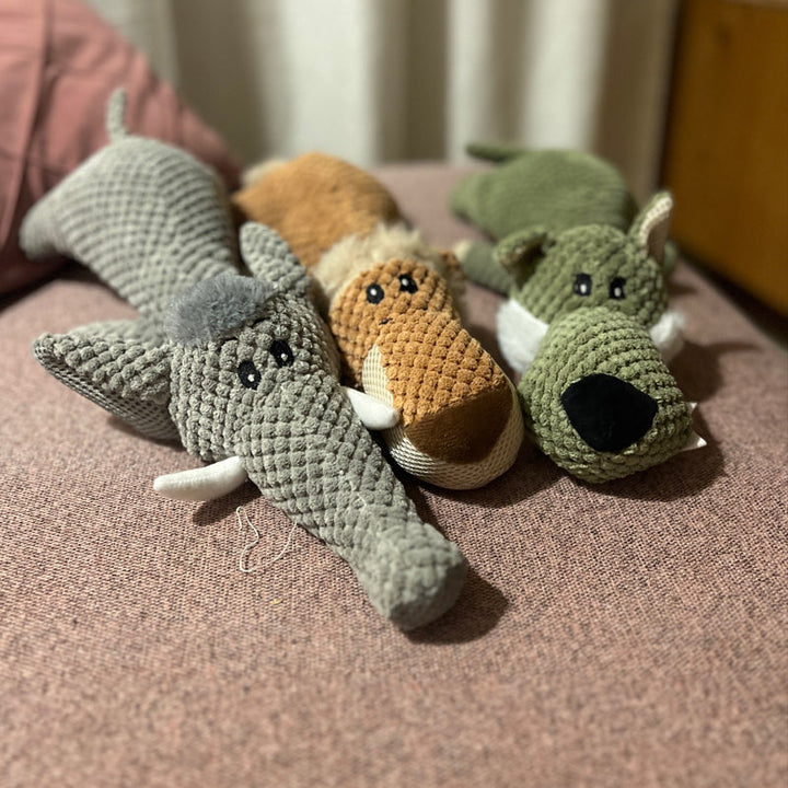 Drei gestrickte Hundespielzeuge in Elefanten-, Fuchs- und Hundedesign auf rosa Sofa.
