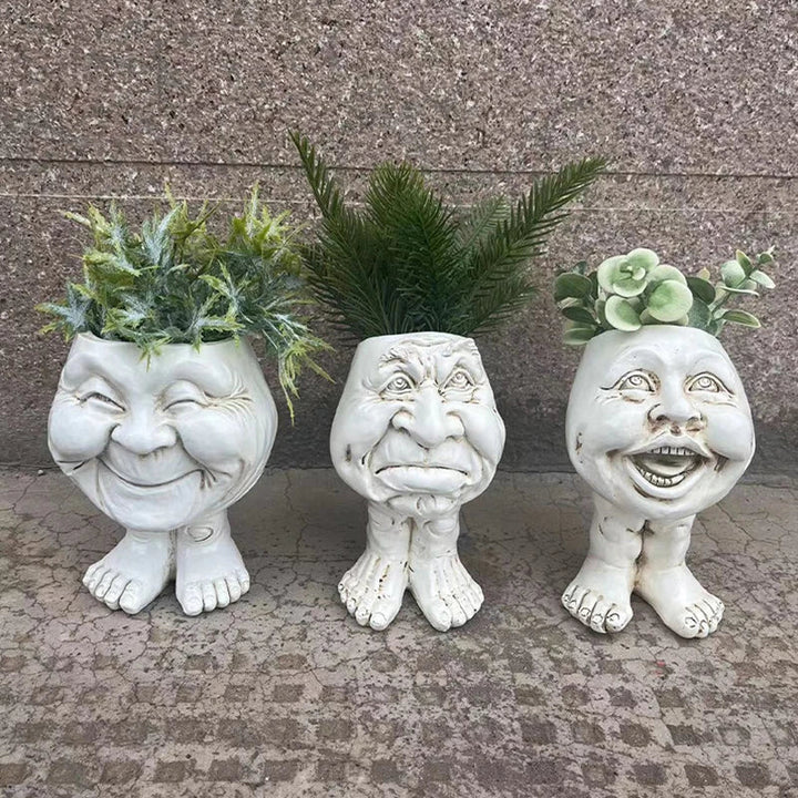 Drei weiße Keramik-Pflanzgefäße mit Gesichtern und Pflanzen, humorvolle Gartendekoration.