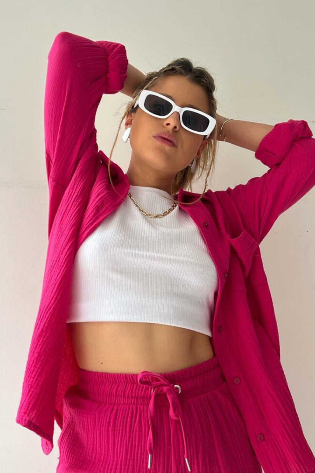 Frau in pinkem Langarmhemd und Shorts, weißes Top, Sonnenbrille, modisch, lässig.