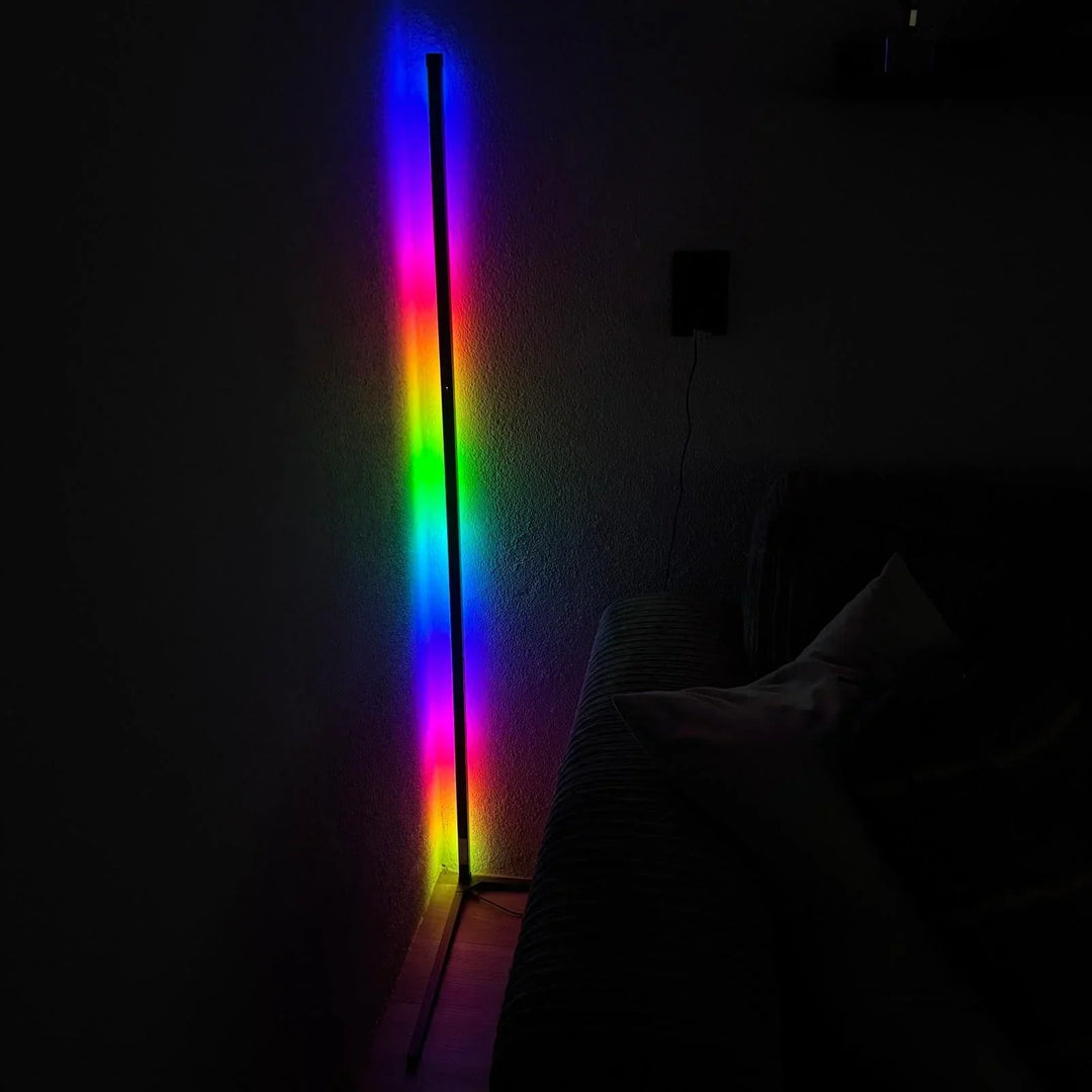 Lampa v tmavém pokoji svítí vícebarevným přechodem od modré přes zelenou a žlutou po růžovou, vedle pohovka. 6