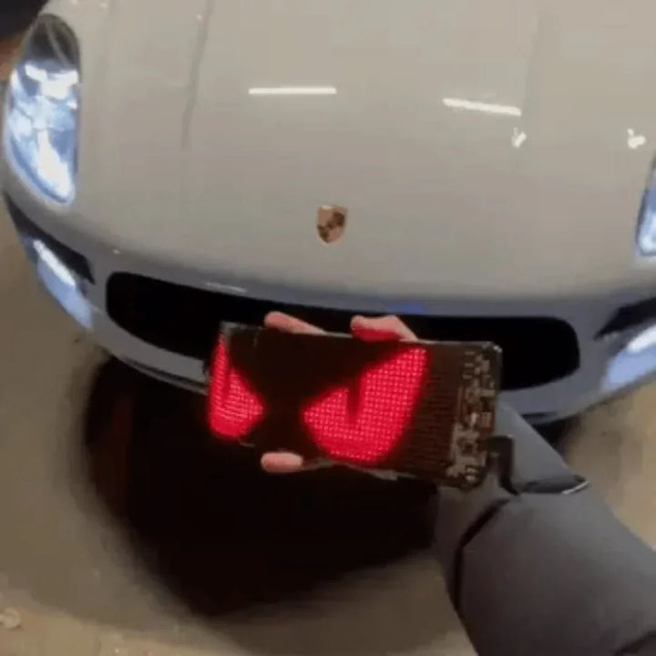 Hand hält LED-Display mit roten Augen vor weißem Porsche, Autozubehör, Beleuchtung.