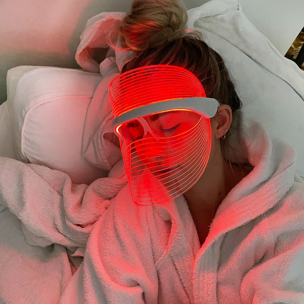 Frau trägt LED-Gesichtsmaske in Rot, Entspannung, Hautpflege, Wellness, Schlaf, Bademantel.