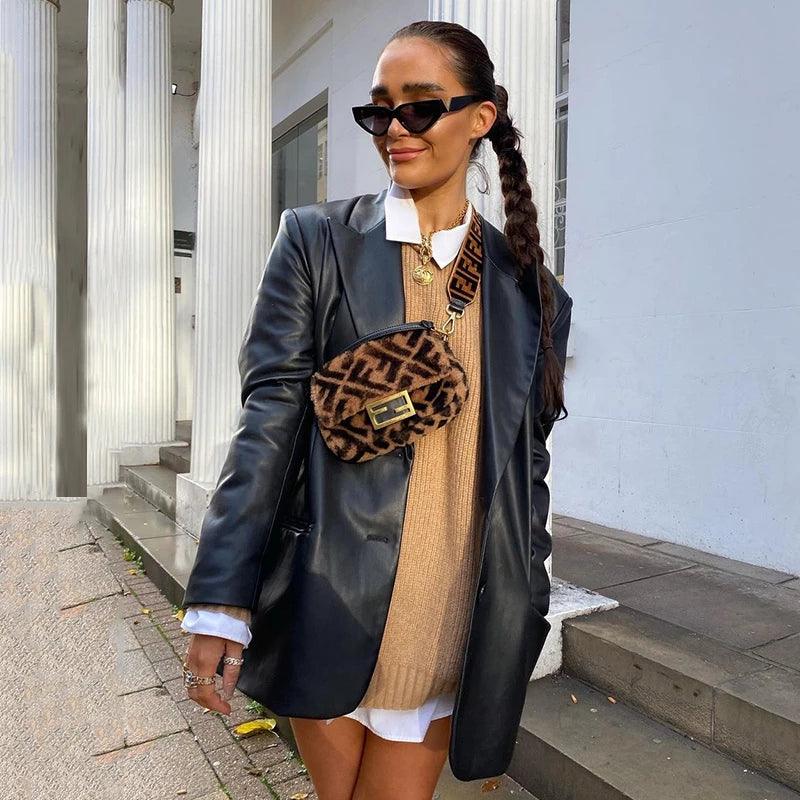 Frau in schwarzer Lederjacke, braunem Pullover, Sonnenbrille, mit gemusterter Umhängetasche.