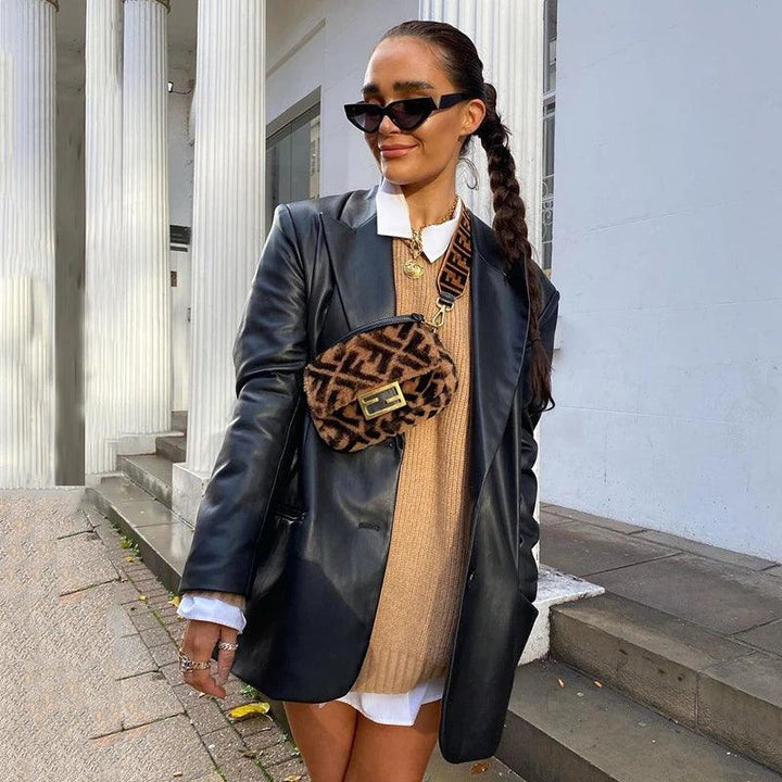 Frau in schwarzer Lederjacke, braunem Pullover, Sonnenbrille, mit gemusterter Umhängetasche.