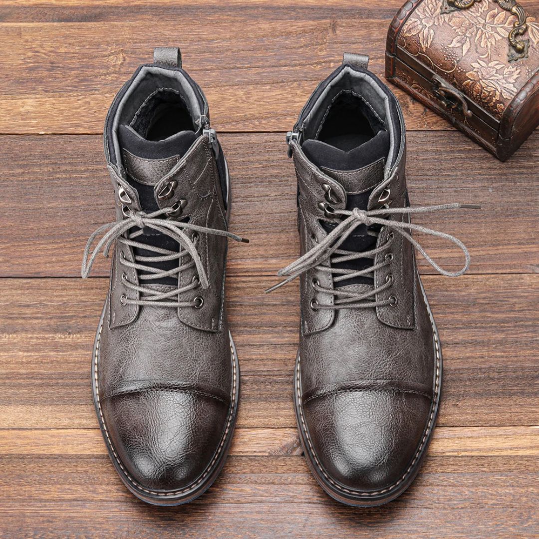 Graue Herrenstiefel aus Leder mit Schnürung auf Holzboden, modisch und robust.