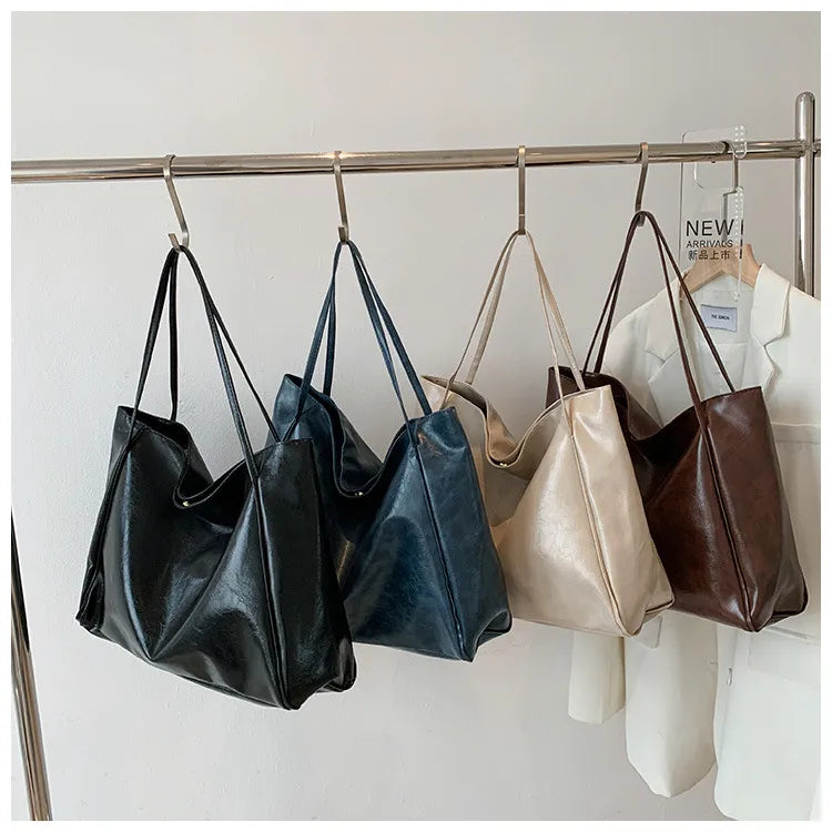 Vier Ledertaschen in Schwarz, Blau, Beige und Braun an Kleiderstange hängend.