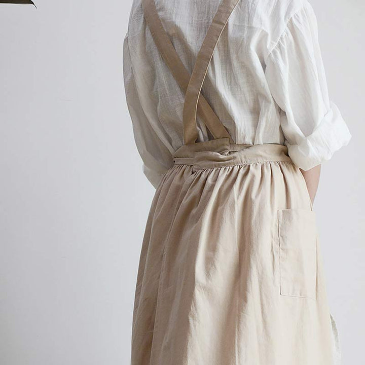 Frau in weißer Bluse und beiger Schürze mit Trägern, Rückansicht, minimalistischer Stil.