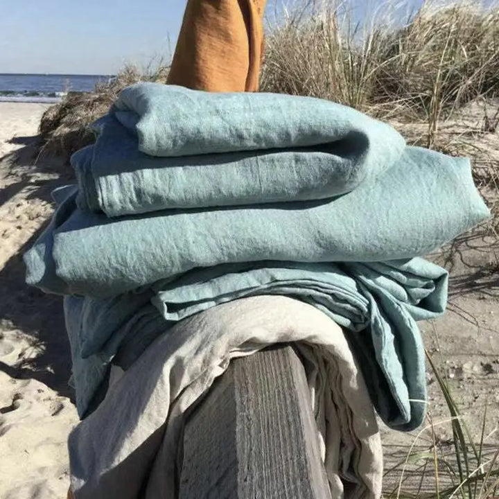 Gestapelte Leinenbettwäsche in Blau und Beige am Strand, nachhaltige Heimtextilien.