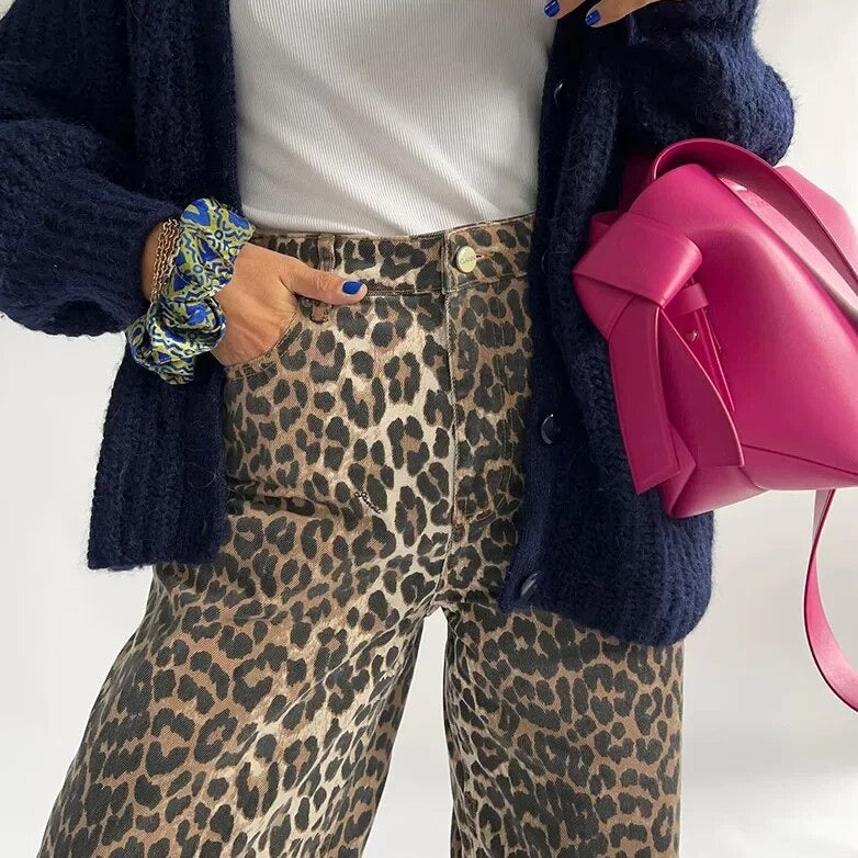 Frau in Leopardenhose, weißem Top, dunkelblauer Strickjacke, pinker Tasche, modisch, trendy.