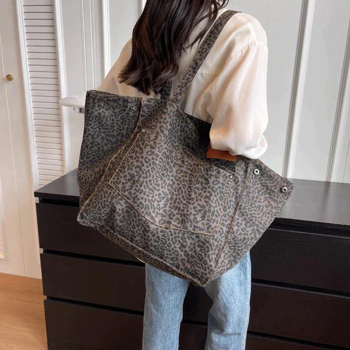 Frau mit großer, grauer Leopardenmuster-Tasche aus Stoff, lässiger Stil, modisch, praktisch.