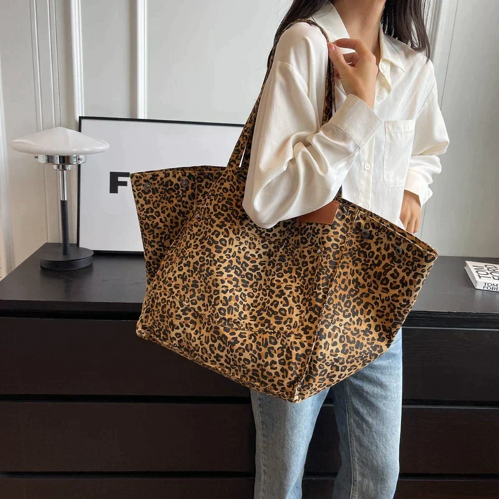Frau mit großer Leopardenmuster-Tasche, weißes Hemd, Jeans, moderne Inneneinrichtung.