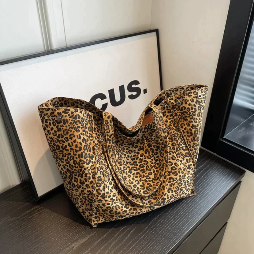 Leopardenmuster-Handtasche aus Stoff auf schwarzem Tisch vor gerahmtem Bild.