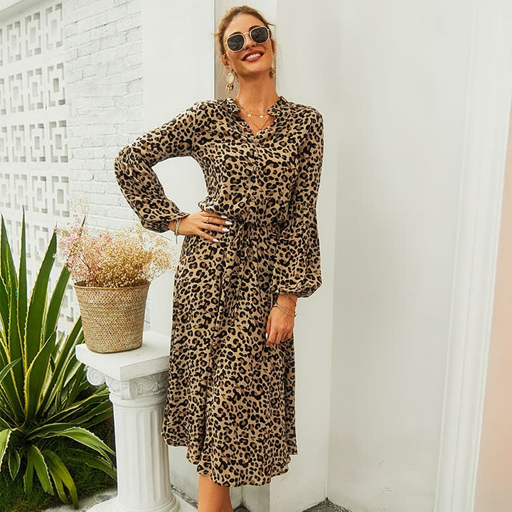 Frau in langem, gepunktetem Leopardenkleid, Sonnenbrille, lächelnd, draußen stehend.