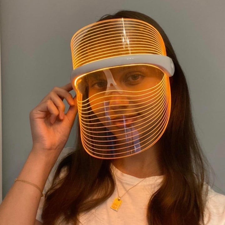 Frau mit leuchtender LED-Gesichtsmaske, orange, futuristisch, Hautpflege, modisch.