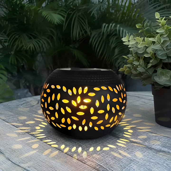 Schwarze Solarleuchte mit Blattmuster, beleuchtet, auf Holztisch im Garten, dekorative Beleuchtung.