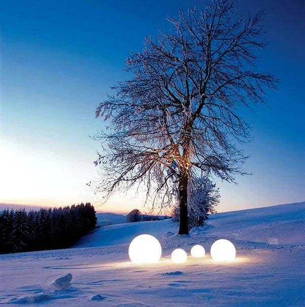 Leuchtende Kugeln im Schnee vor einem Baum bei Sonnenuntergang, Winterlandschaft, stimmungsvoll.
