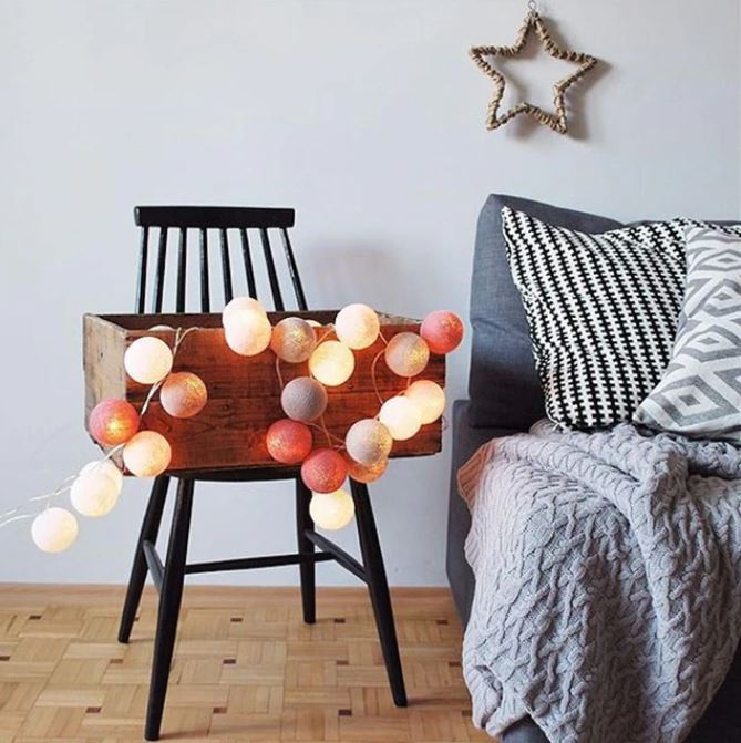 Schwarzer Stuhl mit Holzbox, dekoriert mit bunten Lichterketten, neben grauem Sofa und Kissen.
