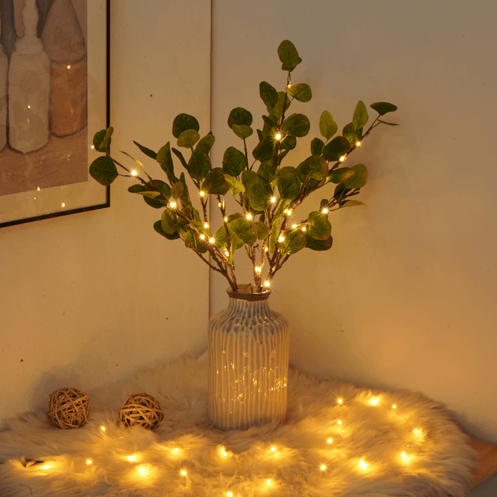 Vase mit grünen Zweigen und Lichterkette, dekorative Beleuchtung, gemütliches Wohnzimmer-Dekor.