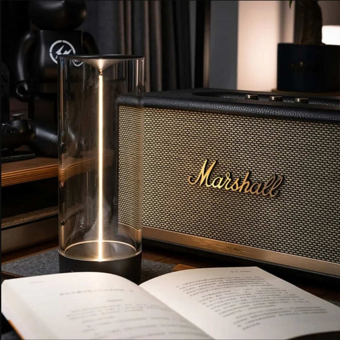 Transparente Tischlampe mit zylindrischem Glas, neben Marshall-Lautsprecher, modernes Design.
