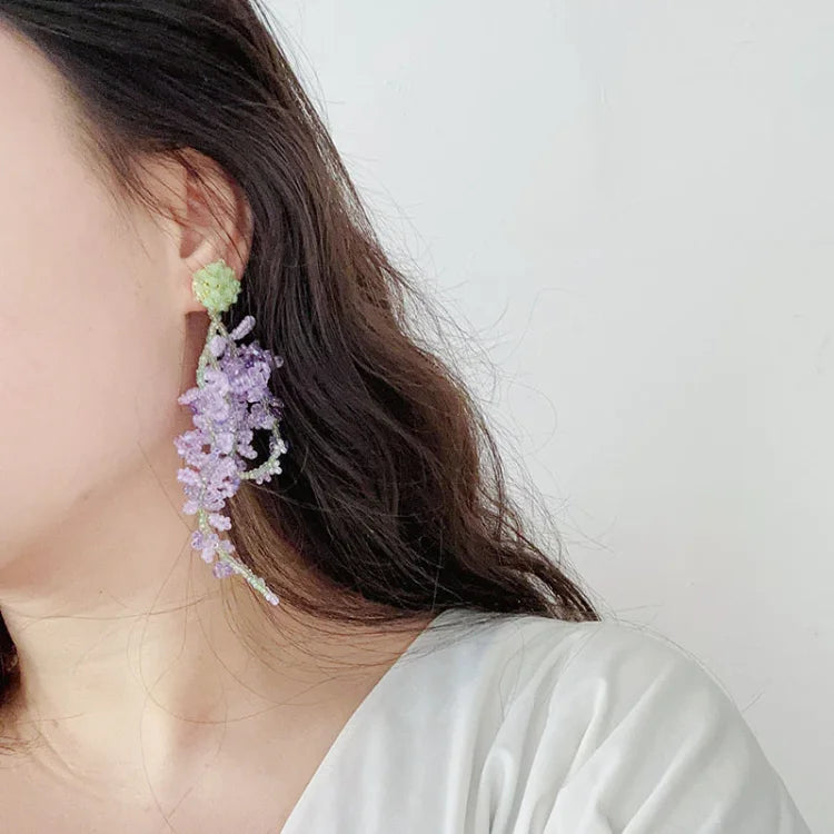 Frau mit lila Blumenohrring, handgefertigt, modisch, Statement-Schmuck, elegant.