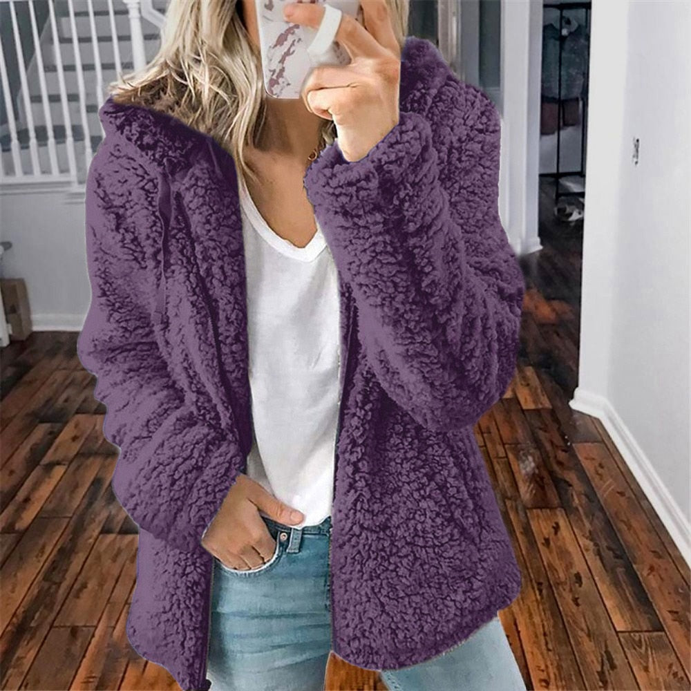 Frau in lila Teddyfelljacke, weißem T-Shirt und Jeans in modernem Innenraum.