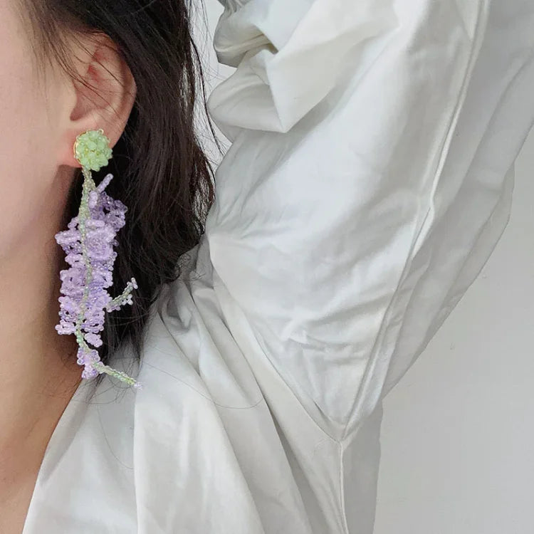 Frau mit handgefertigtem Ohrring aus lila und grünem Perlen, elegantes Schmuckdesign.