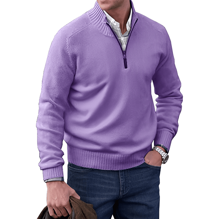 Mann in lila Pullover mit Reißverschluss, weißem Hemd, blauer Jeans, hält braune Jacke.