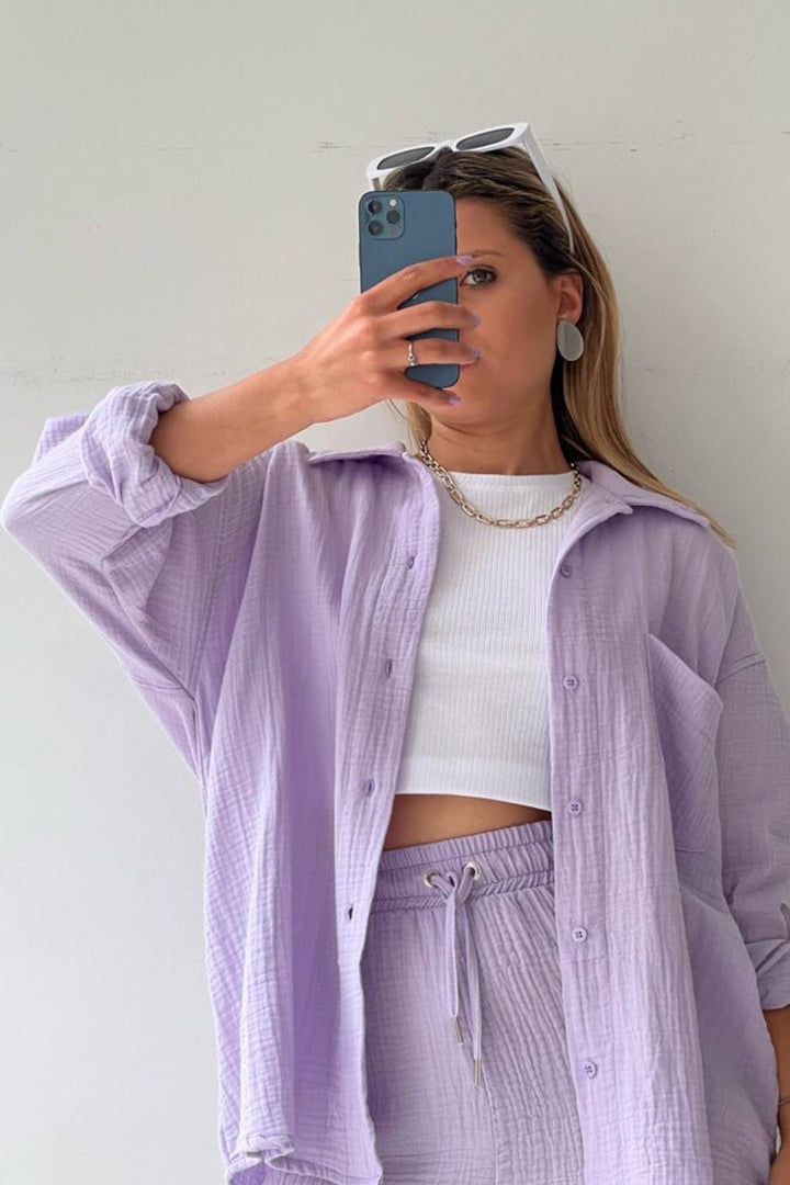 Frau in lila Langarmhemd und Shorts-Set, weißes Top, Smartphone, Sonnenbrille, modisch.
