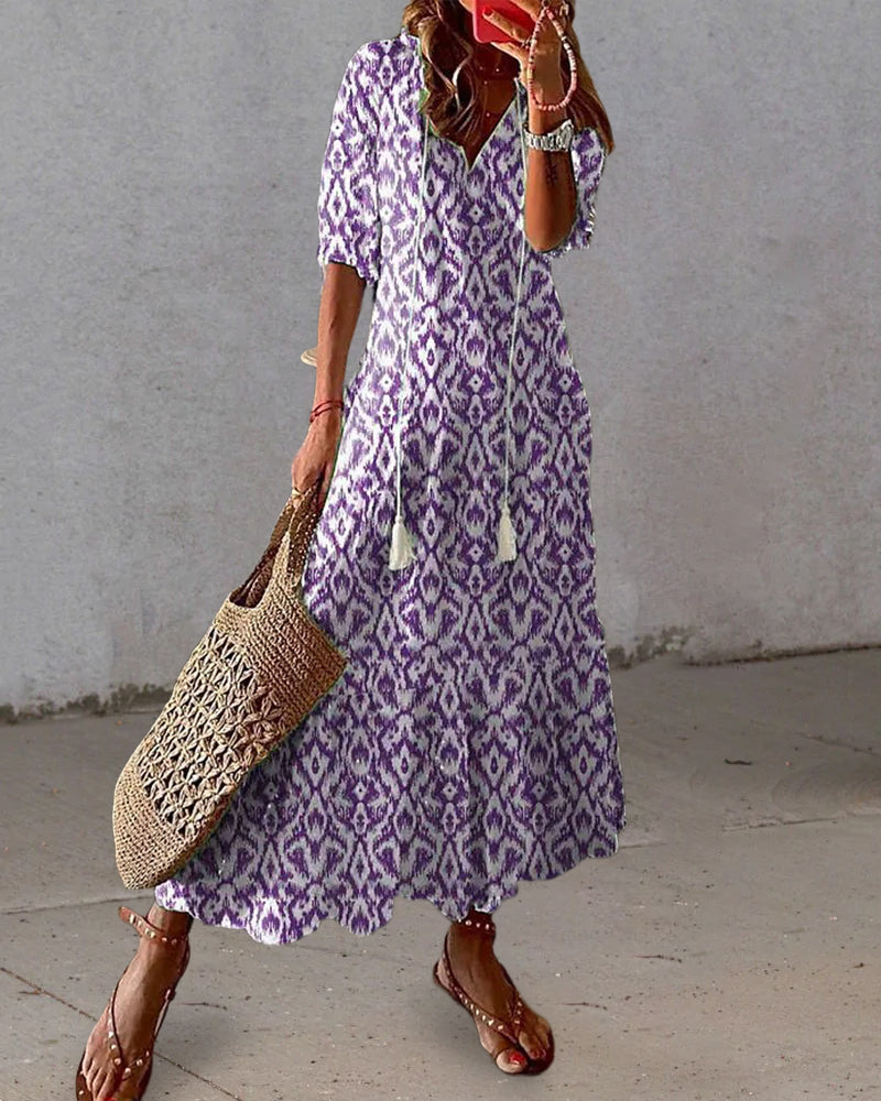 Frau in lila Boho-Kleid mit Ethno-Muster, Strohtasche, Sandalen, Sommermode.