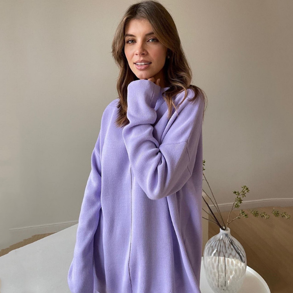 Frau in lila Oversize-Pullover, lässige Mode, gemütlicher Look, Wohnzimmer-Hintergrund.