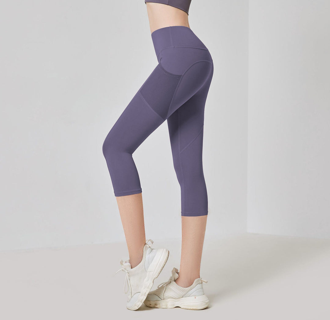 Frau in lila Sportleggings, knielang, mit weißen Turnschuhen, Fitnessmode, seitliche Ansicht.