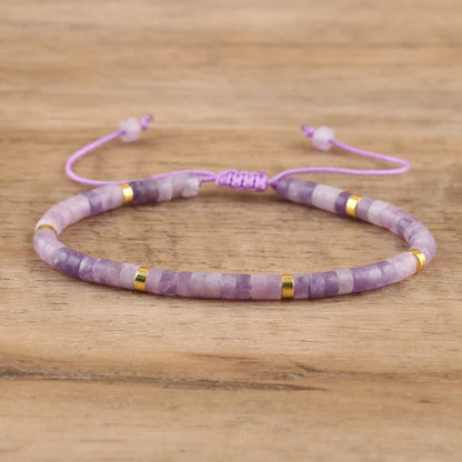 Lila Armband aus Amethyst und Goldperlen, verstellbar, handgefertigt, auf Holzuntergrund.