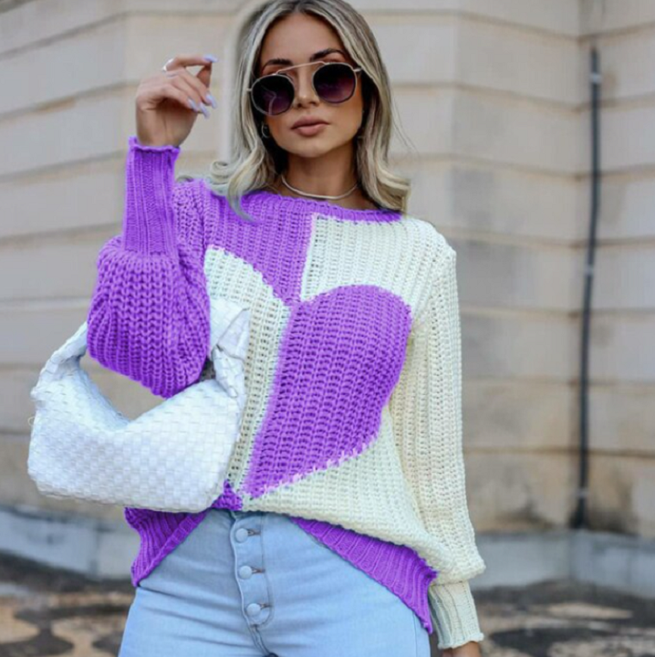 Frau in lila-weißem Strickpullover mit Herzmuster, Sonnenbrille und weißer Tasche.